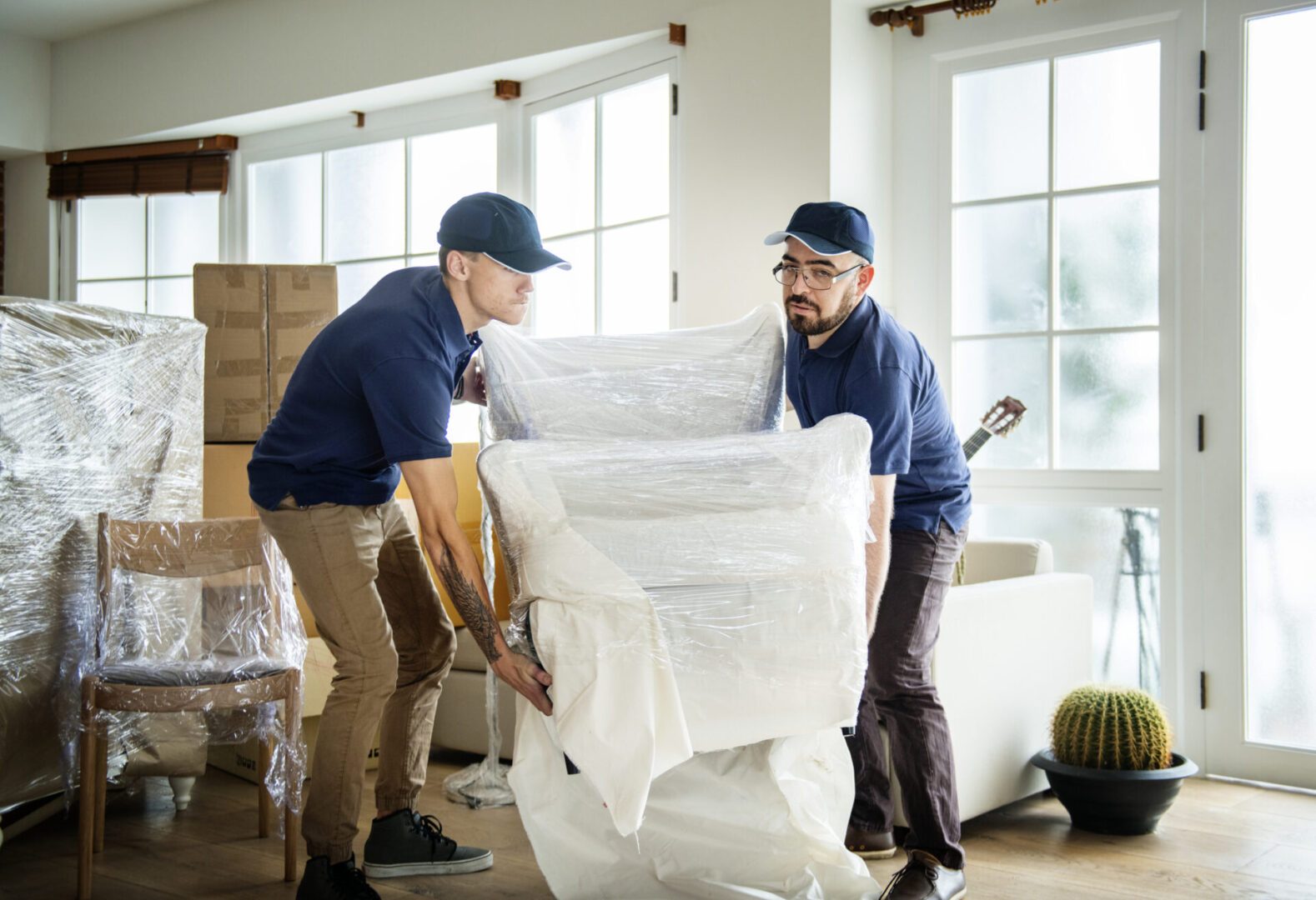 Movers carrying wrapped furniture in living room.